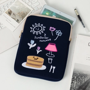 Detail of dark blue laptop sleeve featuring sunflower pancake embroidery on a white desk