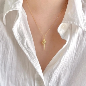 Close-up of golden conch shell pendant on a fine cross chain worn by a model