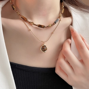 Close-up of double layer gold plated necklace featuring tiger eye stone on a white suit