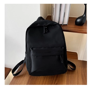 Detail view of a black minimalist nylon backpack on a wooden table in a lifestyle setting