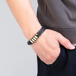 Men's braided black leather bracelet with gold metal bar accent on model wrist