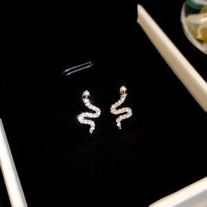 Macro shot of silver snake-shaped earrings with shimmering crystals on black velvet
