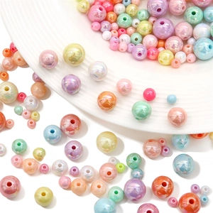 Colorful acrylic round beads in various sizes on a textured white plate for DIY jewelry