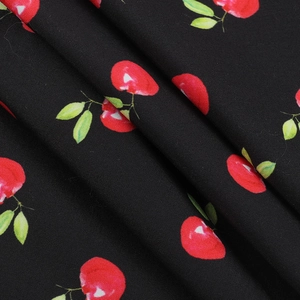 Macro shot of vibrant red cherry print and green leaves on black fabric texture