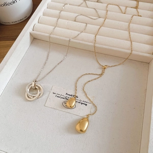 Detail of 18k gold plated teardrop necklace and silver triple ring pendant on velvet tray
