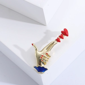 Macro shot of gold hand gesture brooch with red hearts and blue enamel cuff detail
