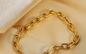 Macro shot of gold paperclip link bracelet on champagne silk fabric with warm lighting