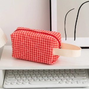 Detail of red checkered quilted cotton makeup bag with woven handle on a desk