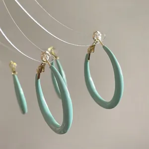 Detail of mint green resin C-shaped hoop earrings with polished gold-tone metal posts