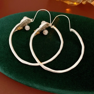 Close-up of silver hoop earrings with small pearl charms on dark green velvet background