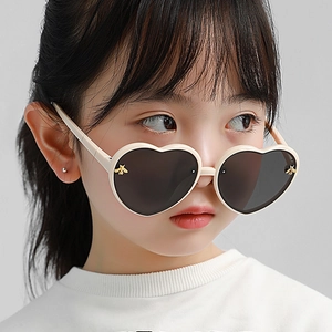 Detail of cream heart-shaped sunglasses featuring gold bee accent on dark lenses