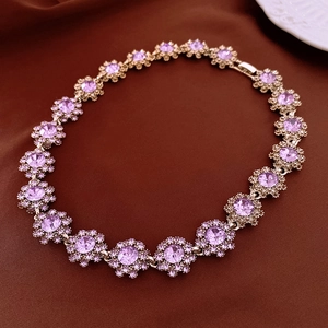 Detailed close-up of golden floral necklace with purple gemstones on brown fabric background