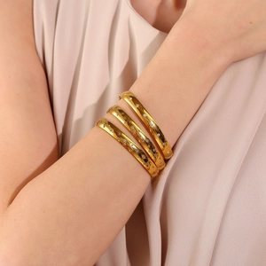 Detail showing three gold bangles with star engravings and white zircons on a wrist