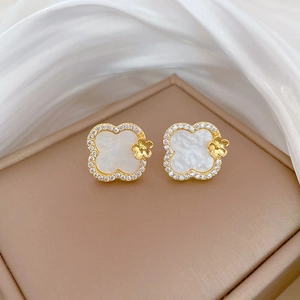Close-up of golden four-leaf clover stud earring with white shell and pavé diamonds
