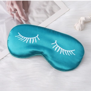 Detailed view of blue silk sleep mask with white eyelash print on soft white plush surface