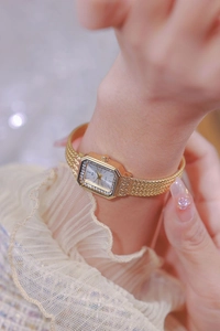 Close-up of gold square watch with rhinestone bezel on woven mesh strap on female wrist