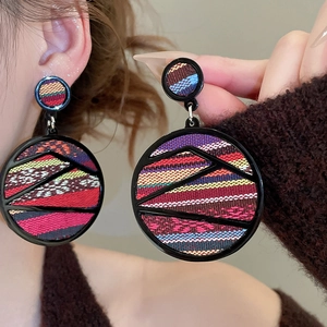 Detail of round acrylic bohemian earrings with colorful woven patterns on a model