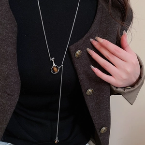 Close-up of a silver Y-shaped sweater necklace with a brown tiger eye stone pendant