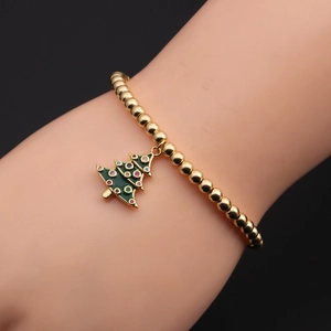 Dettaglio del bracciale con perline dorate e ciondolo albero di Natale verde sul polso