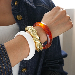 Stack of white resin, twisted gold metal, and amber tortoise shell bangle bracelets