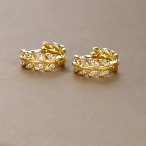 Macro shot of gold leaf earrings with small white crystals and detailed metal texture