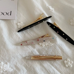 Detail of four-piece acetate hair clips with colorful rhinestones on a white fabric base