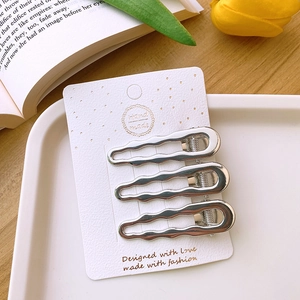 Close-up of three wavy silver metal hair clips displayed on a handmade paper card