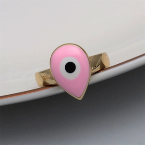 Detailed close-up of pink enamel evil eye ring with gold band on white porcelain edge