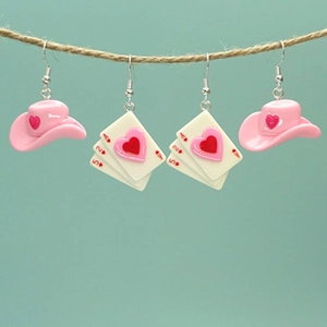 Detail of pink cowboy hat and playing card heart resin earrings hanging on a rope