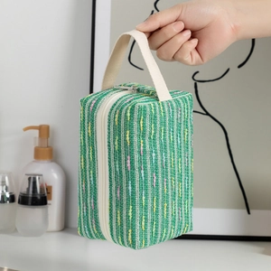Close-up of green woven cosmetic bag with colorful stripes and sturdy canvas handle