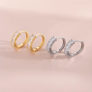 Gold and silver hoop earrings with baguette cubic zirconia inlay on a pink background