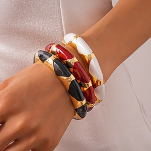 Close-up of three chunky enamel bangles in black, red, and white with metallic finish