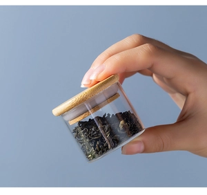 Close-up of portable glass tea canister with bamboo lid being held by hand