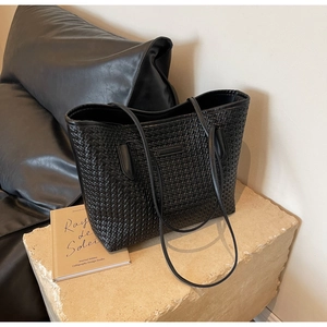 Detailed view of black woven faux leather tote bag on beige stone with accessories