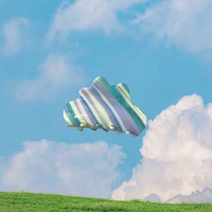 Cloud-shaped iridescent acetate hair claw with pastel stripes against a blue sky background
