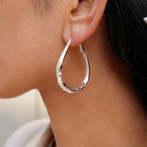 Macro shot of silver teardrop twisted hoop earring on a model for modern style