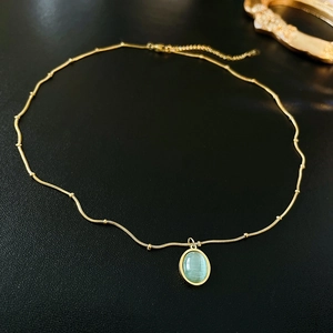 Macro detail of gold-plated oval green gemstone pendant necklace on black background