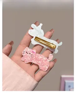 Detailed view of pink and white acetate cat hair clips with golden metal duckbill clips