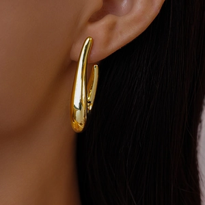 Macro view of fluid gold-toned droplet earring with polished metallic surface finish