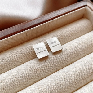 Macro detail of silver rectangular earrings with engraved charm text and brushed metal texture
