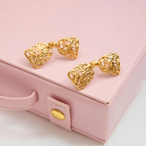 Golden lace cutout bow earrings displayed on a pink jewelry box with metallic texture
