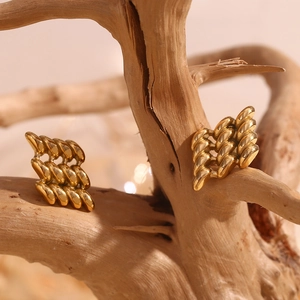 Detail of 18K gold-plated geometric earrings with woven texture on a natural wood branch
