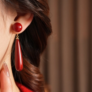 Close-up of elegant dark red teardrop earrings worn by a model against a textured background