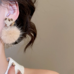 Detail view of heart-shaped leopard print stud with a fluffy beige pompom earring