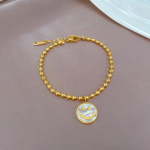 Goldenes Titanstahl-Perlenarmband mit Smiley-Anhänger aus Perlmutt auf lila Lederhintergrund