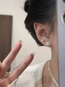 Macro shot of dandelion firework earrings and white pearl stud on ear with necklace