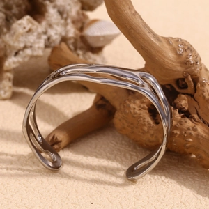 Detailed view of silver wavy hollow open cuff bracelet on natural textured surface