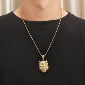 Close-up of a golden owl pendant necklace with a detailed woven chain on a model