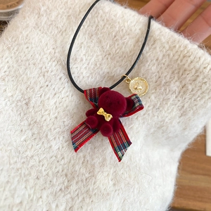 Dettaglio del ciondolo a forma di orsetto bordeaux con fiocco dorato su maglione a maglia
