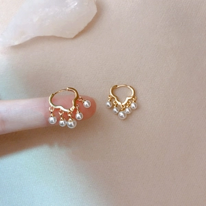 Golden hoop earrings featuring five hanging pearls shown on finger for scale